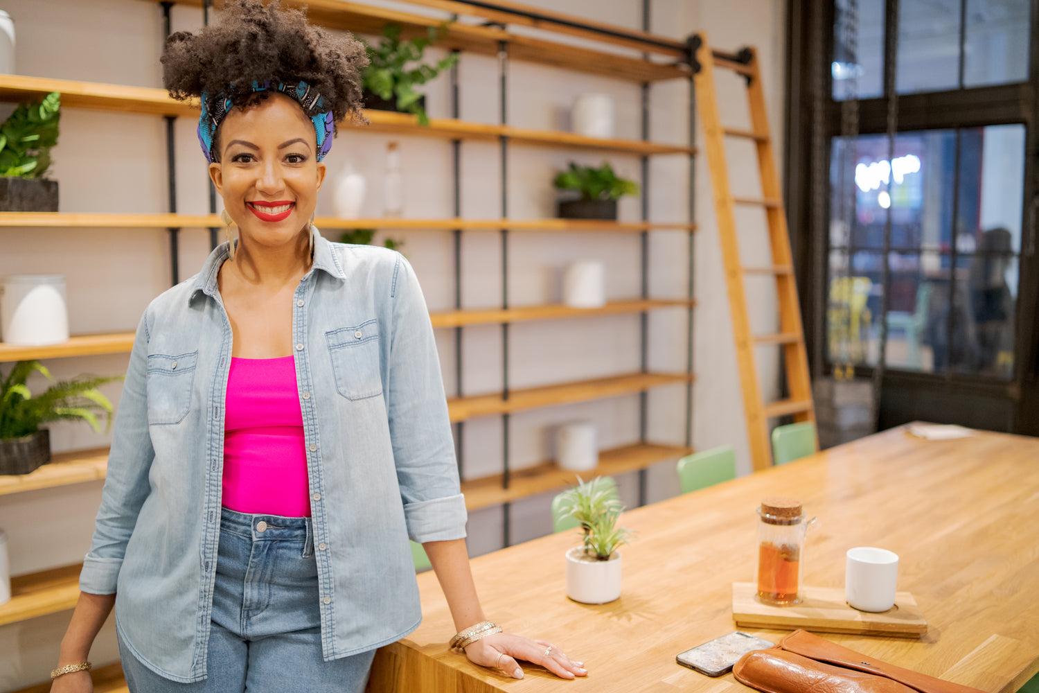 Woman standing in a modern office setting with wooden shelves and plants.
